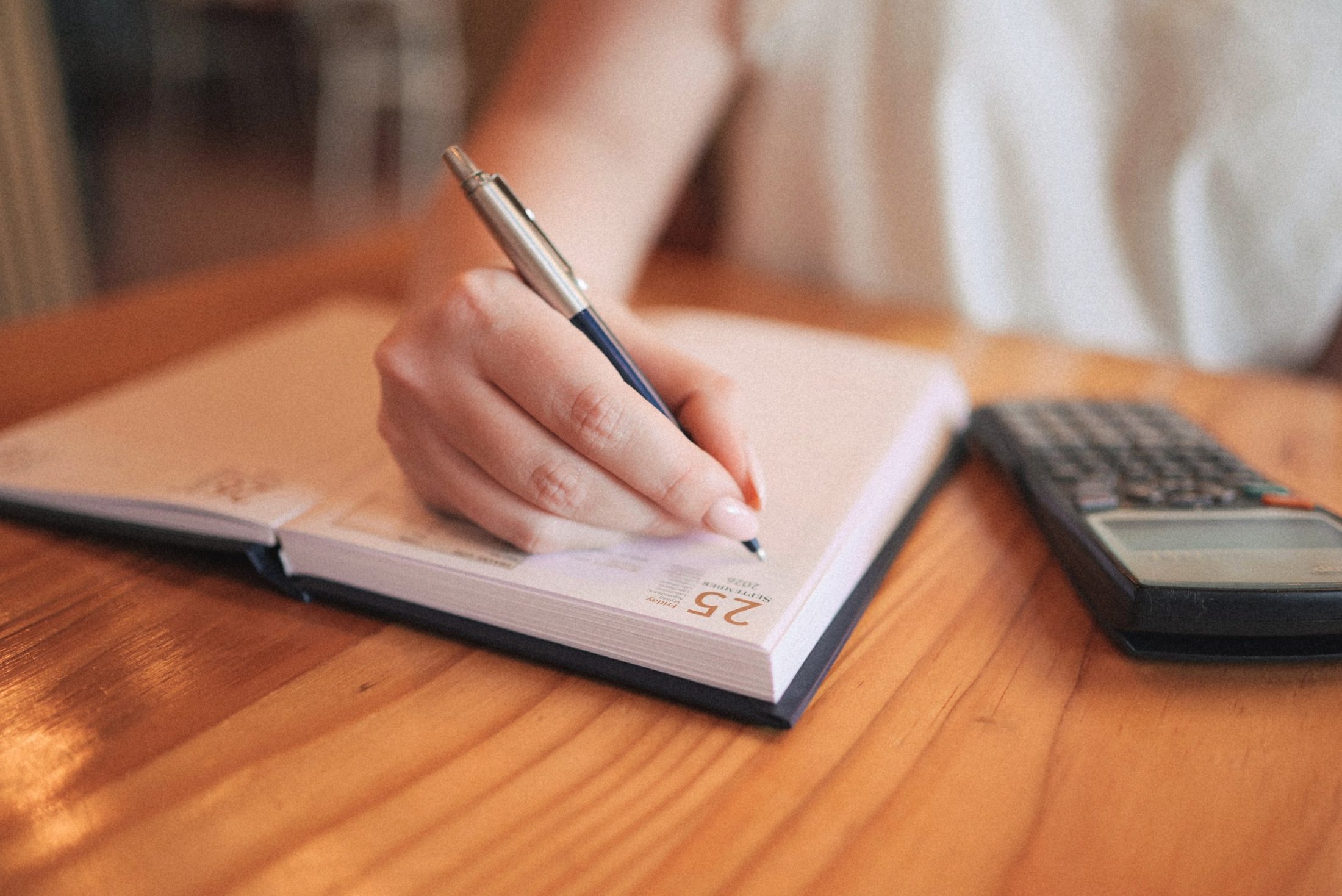 Hand writing in a desk diary beside a calculator