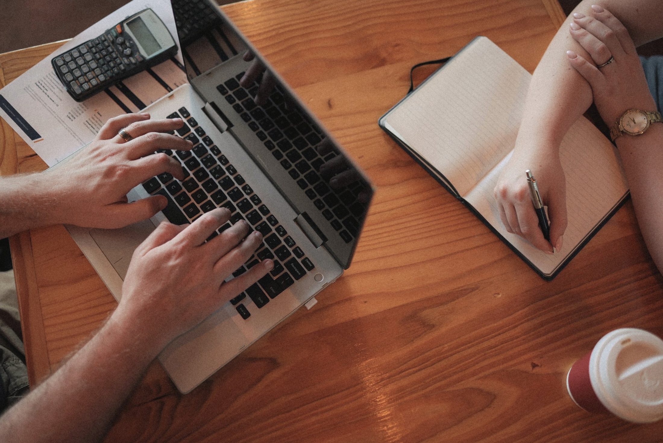 Two people working together at a desk, reviewing figures on a laptop and in a notebook