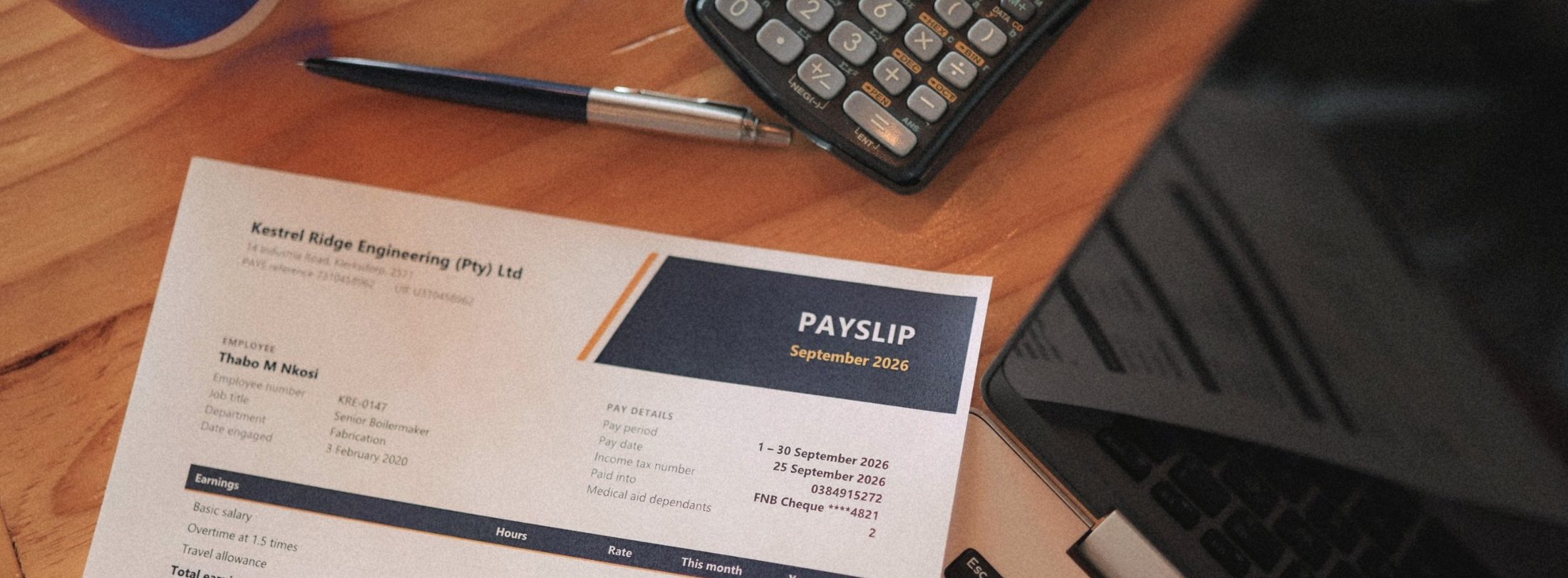 A completed monthly payslip beside a calculator and laptop